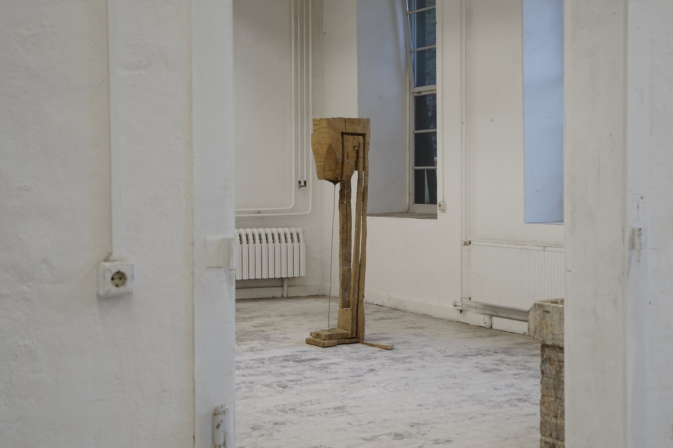 Untitled: a standing wooden figure seen through the doorway of a white studio room